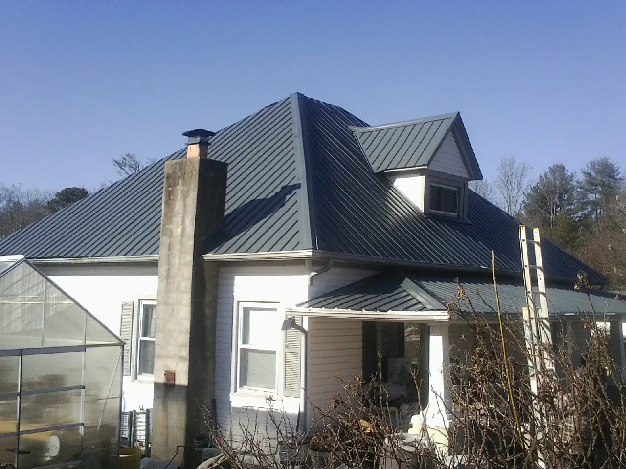 Dark blue standing seam metal roof on a white farmhouse with dormer — Slate & Tile Roof Repair by Roofing Brothers in Mead