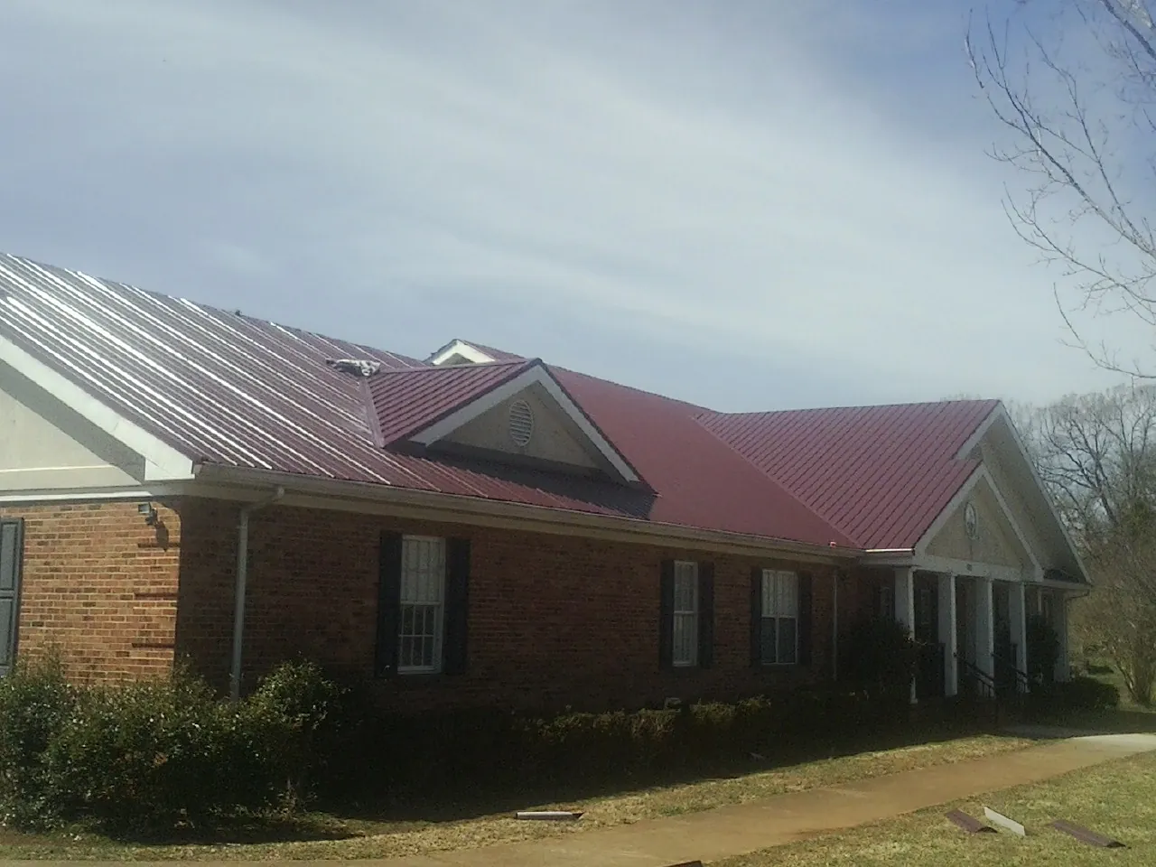 Red metal roof with gabled entries on a long brick building, from a Hail Damage Roof Repair job in Mead