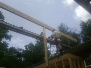 Carpenter setting a ridge beam over a new addition frame in Mead