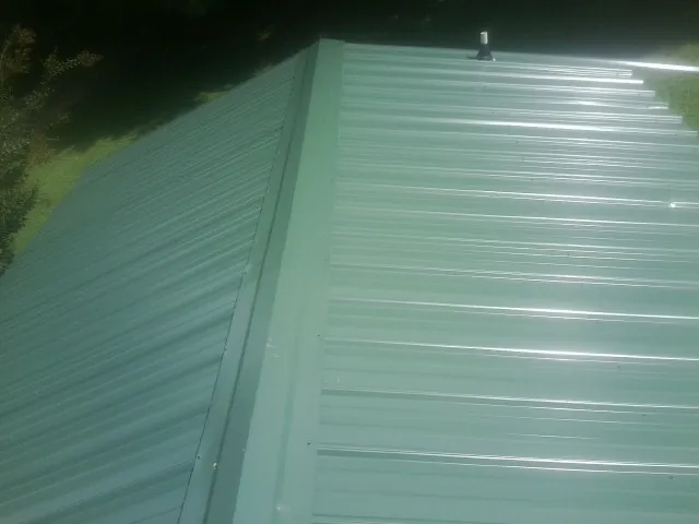 New green metal panels meeting at the ridge of a roof — Flat Roof Repair work by our crew in Mead